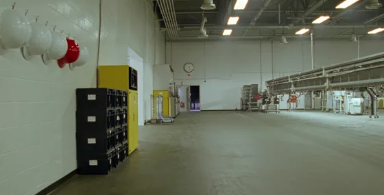 Boş bir fabrika zemininde duvara asılı beyaz baretler arasında tek bir kırmızı baret